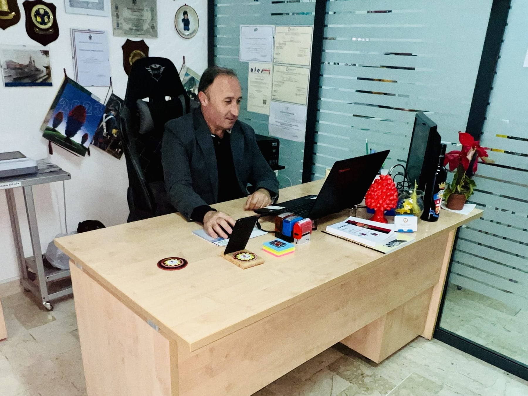 Maurizio Ferrara alla scrivania della sede, davanti alla parete dei riconoscimenti